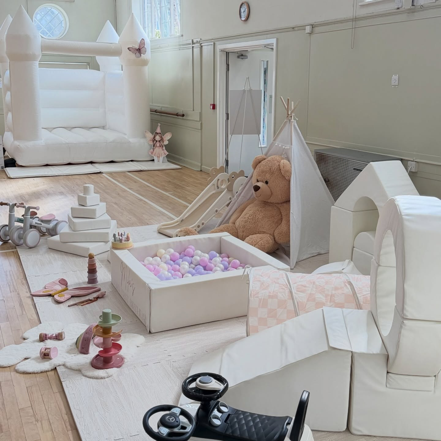 White bouncy castle with pastel pink ball pit, teddy and soft play set